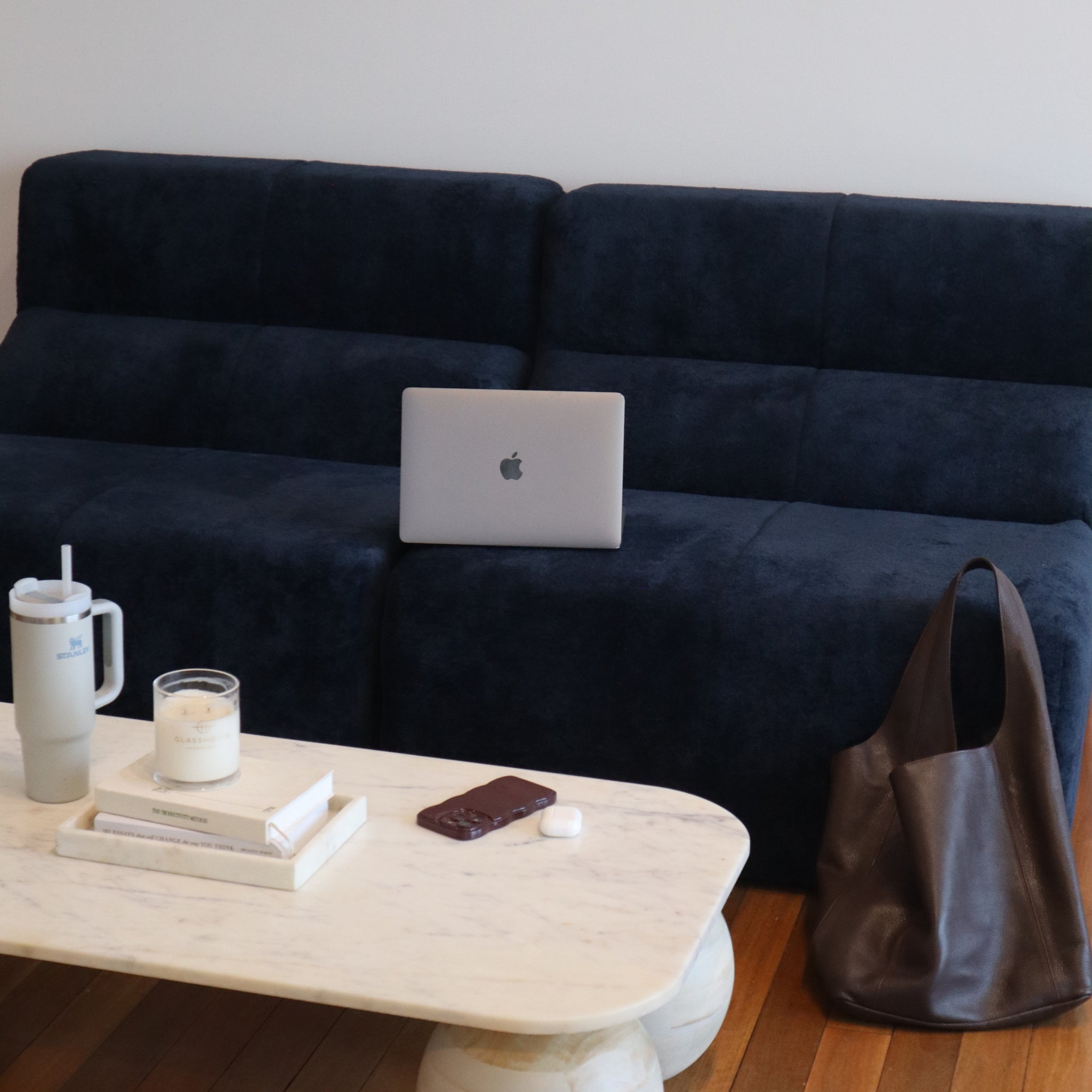 Navy blue sofa with a laptop, coffee cup, and phone on a wooden coffee table.